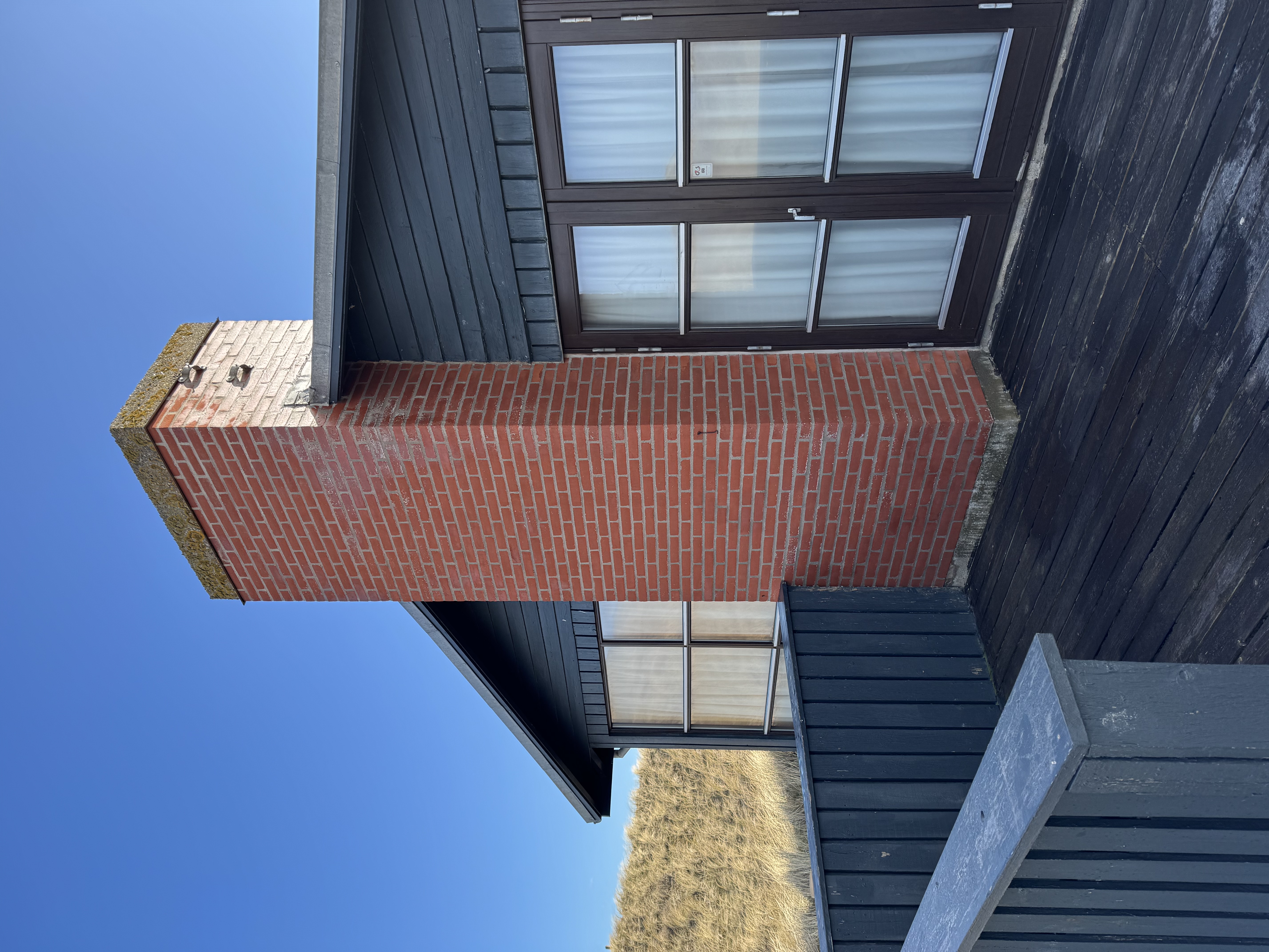 Rødt murstensskorsten på sort træhus under blå himmel